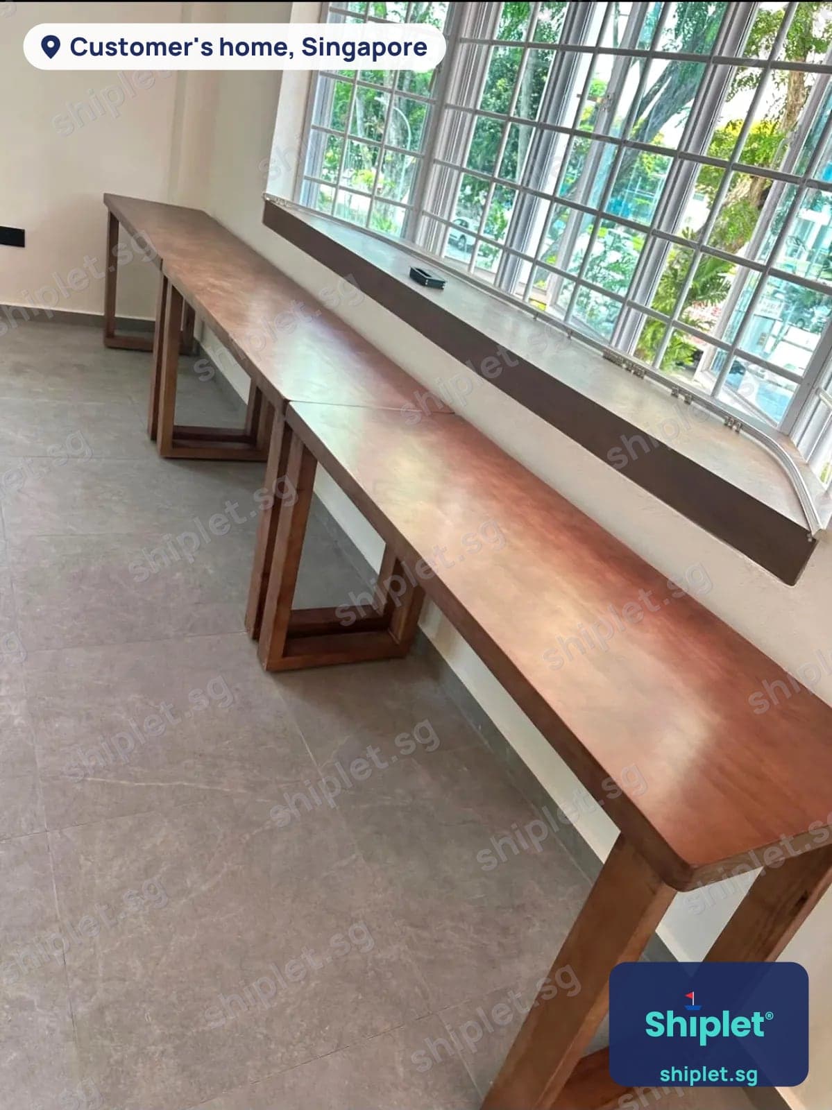 Long solid wood bar table in two sections assembled along a window in a Singapore home