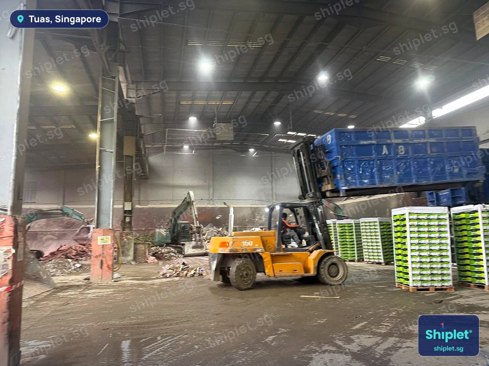 Forklift carrying a blue open-top waste bin across the disposal facility in Tuas