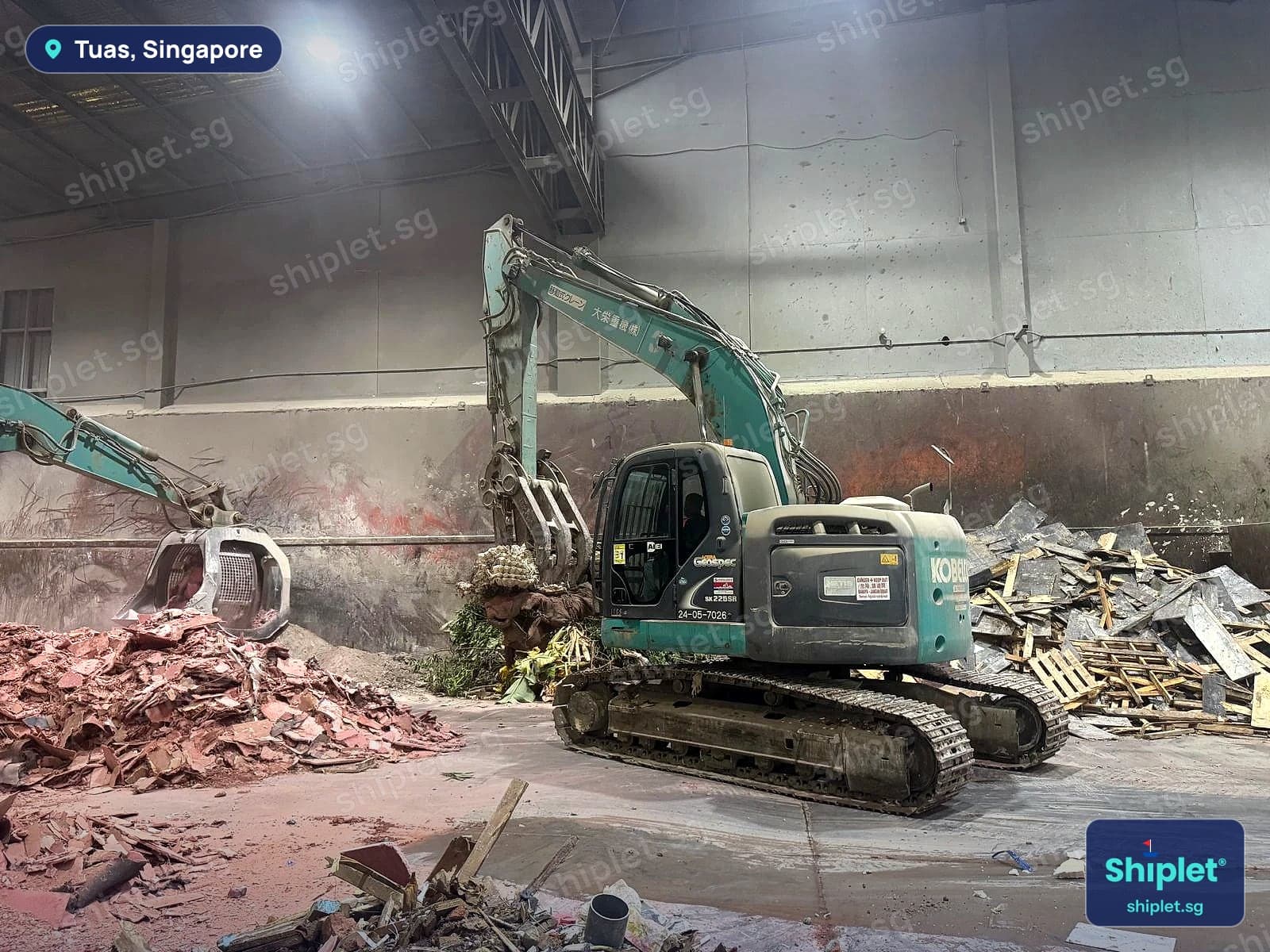 Excavator with a grab beside a pile of broken wooden pallets and crate wood in Tuas, Singapore