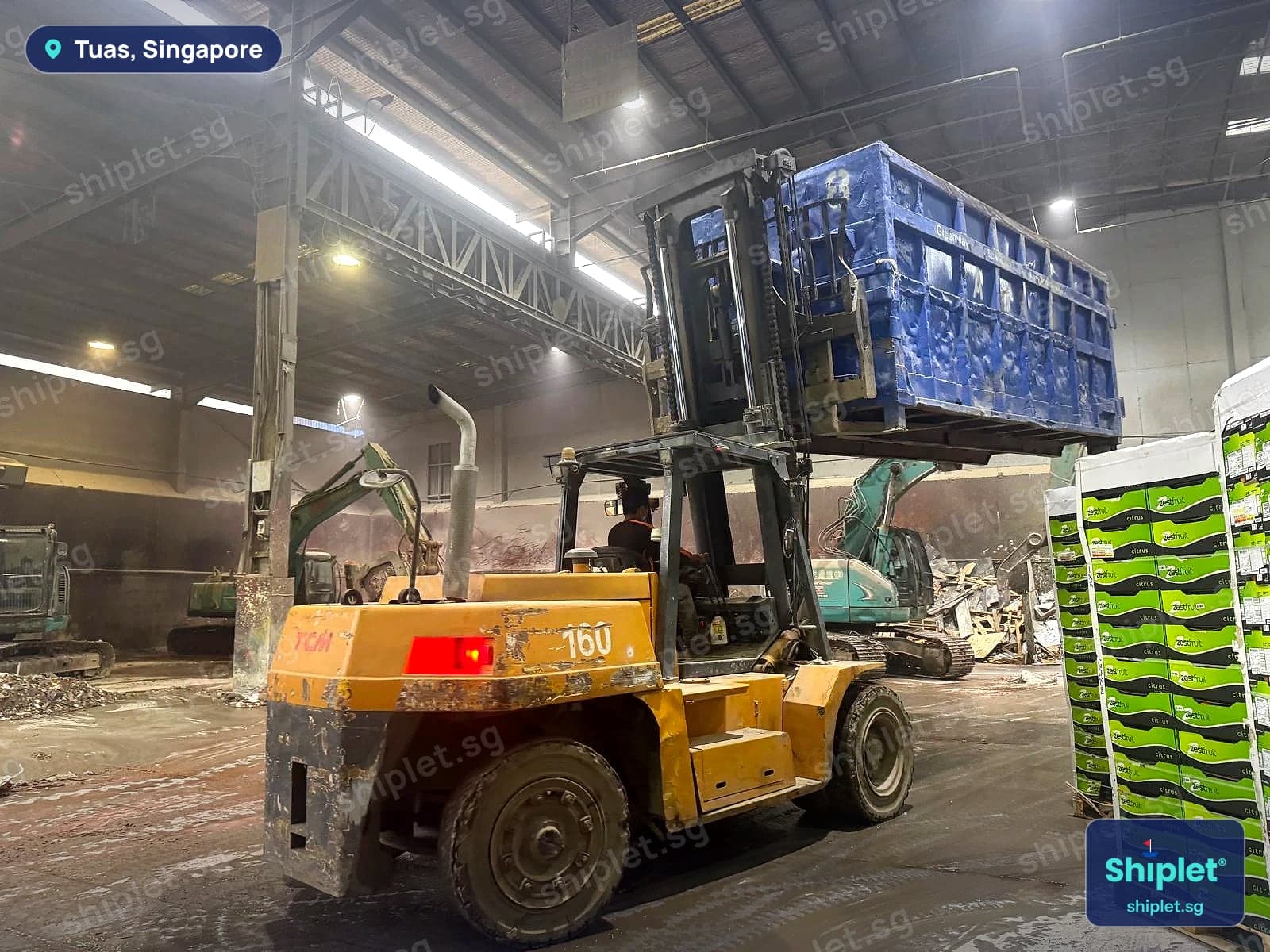 Forklift raising a loaded blue bin beside excavators at a Tuas waste disposal facility
